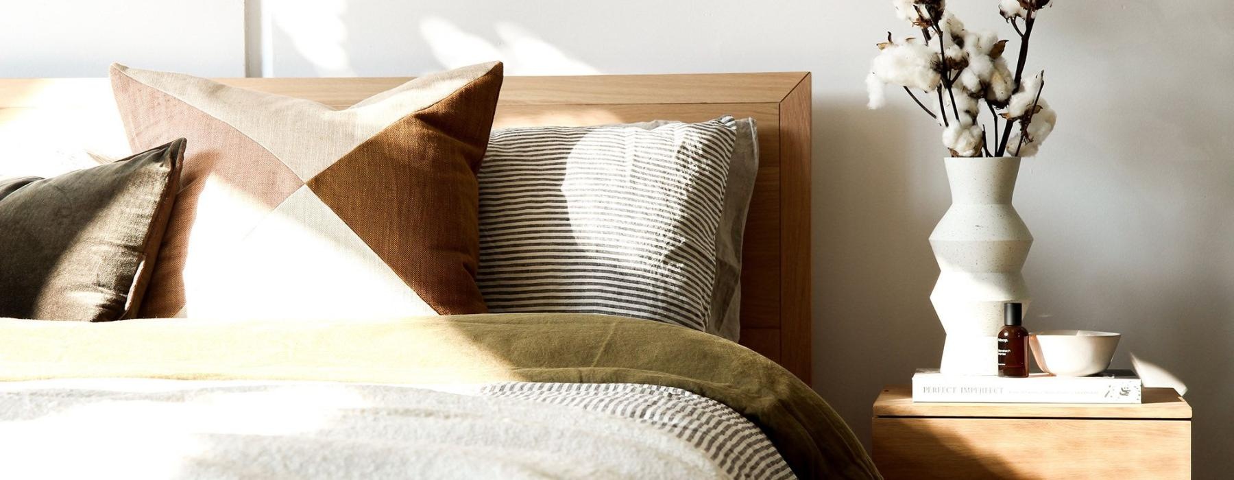 swath of sunlight shines across a well made bed and bedside table with a vase of cotton plants